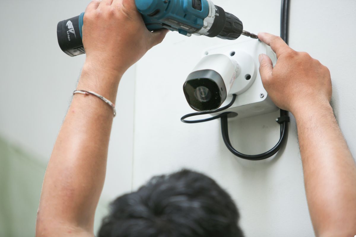 A man drills into a wall to securely attach a camera for surveillance or photography purposes.